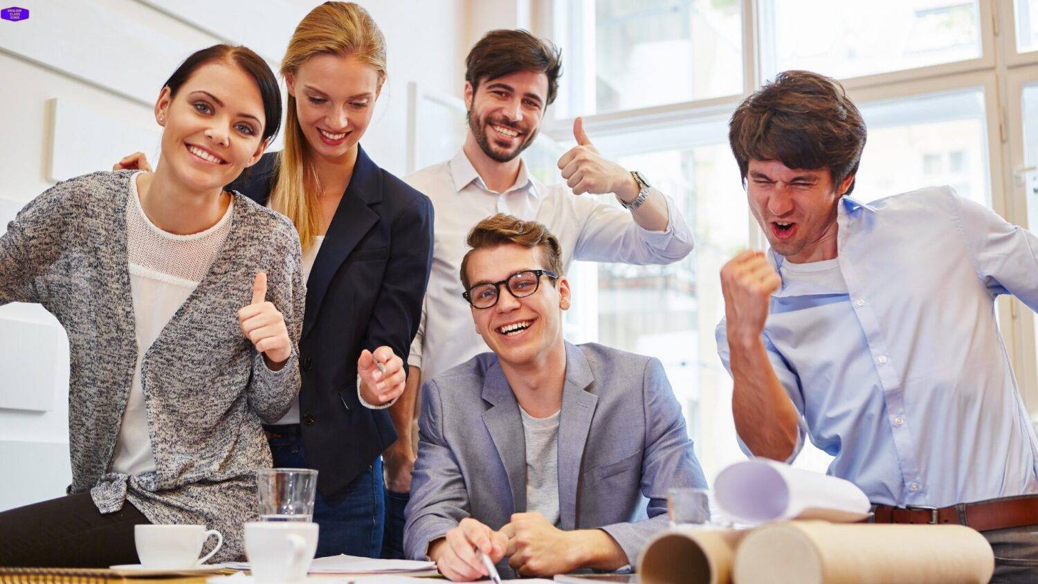 Group of enthusiastic young professionals celebrating success in a collaborative workspace with thumbs up and smiles, conveying excitement and team spirit.