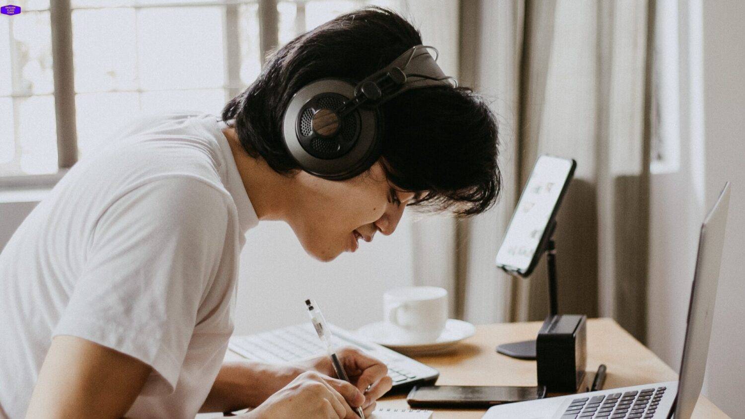 Student with headphones concentrating on an Intermediate English lesson, taking notes to enhance language skills.