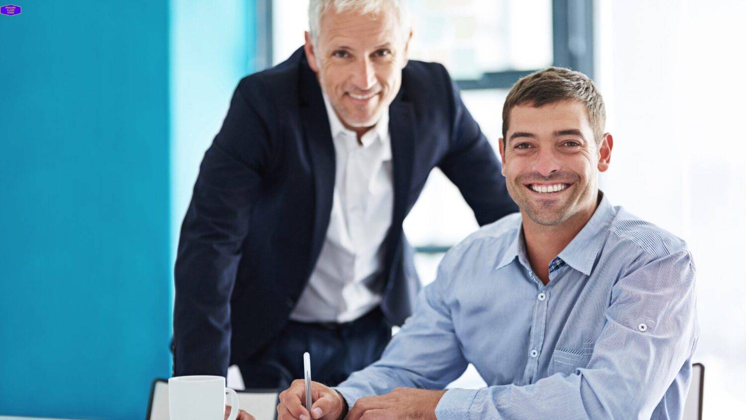 Two smiling professionals, one seated and one standing, symbolizing the supportive and personalized approach of private English classes at English Class CDMX, tailored to meet individual learning goals.