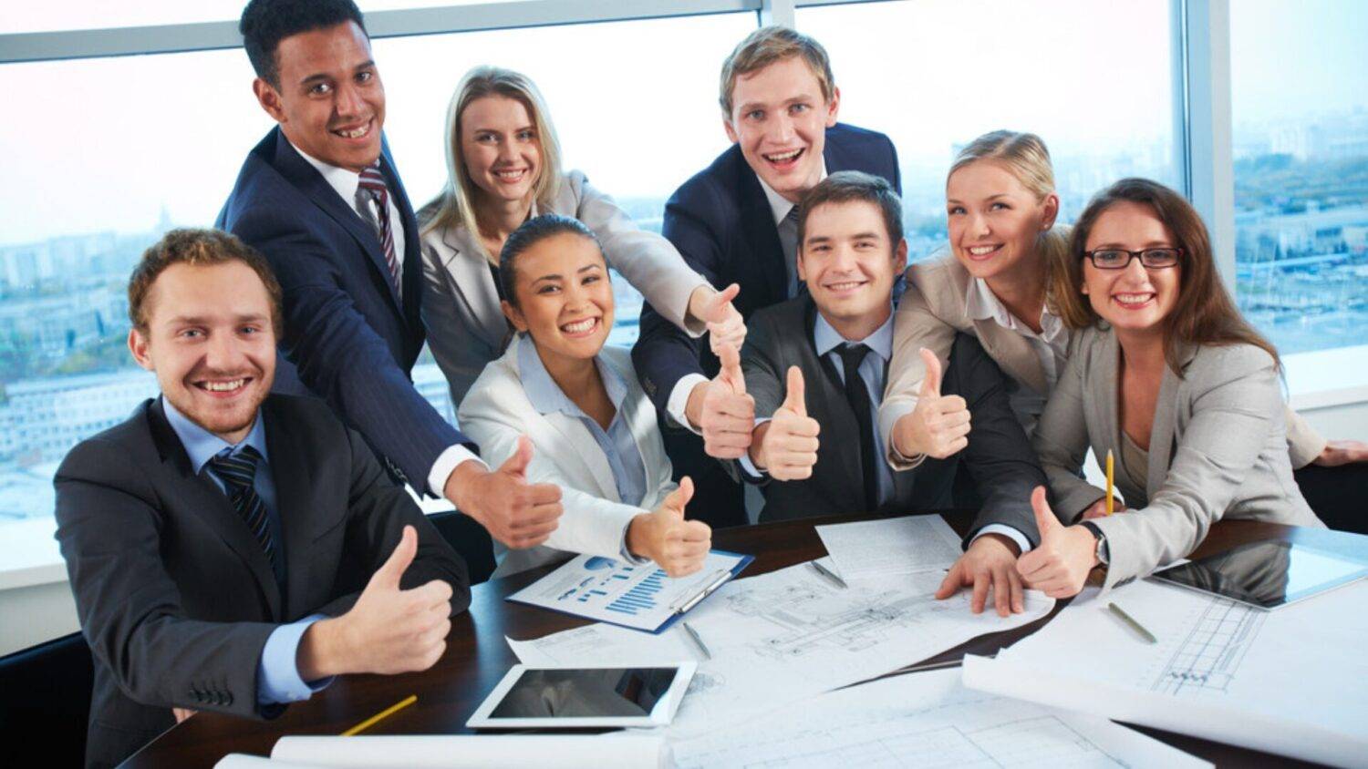 Group of professionals in a business setting giving thumbs up, symbolizing success and confidence gained through advanced English classes