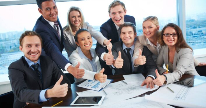 Group of professionals in a business setting giving thumbs up, symbolizing success and confidence gained through advanced English classes